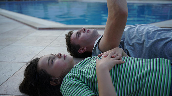 aftersun - a man and young girl laying on their backs on the ground next to a swimming pool