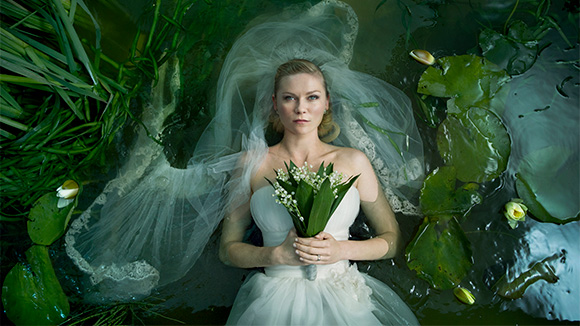 melancholia - beautiful blonde woman wearing wedding dress laying in what appears to be a pond surrounded by plants and foliage