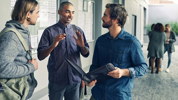 three males students stand talking in a college campus hallway