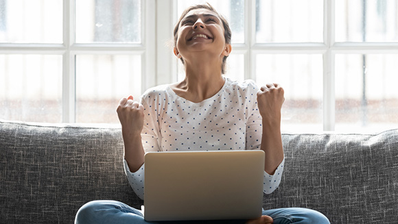 excited young woman sitting cross-legged on couch, laptop on her lap