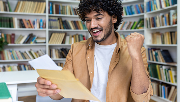 excited young man opening letter and holding fist up in triumph