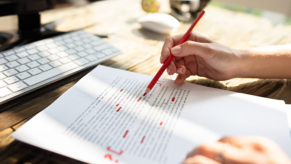 close-up of person proofreading a document, holding a red pen with plenty of edit marks on paper