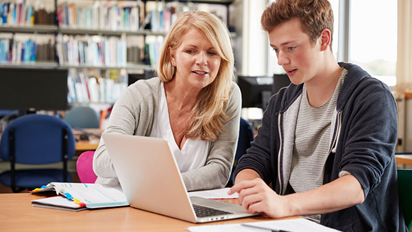 young man having older woman, possibly mom, professor, or counselor, look at his work on a laptop they both look at