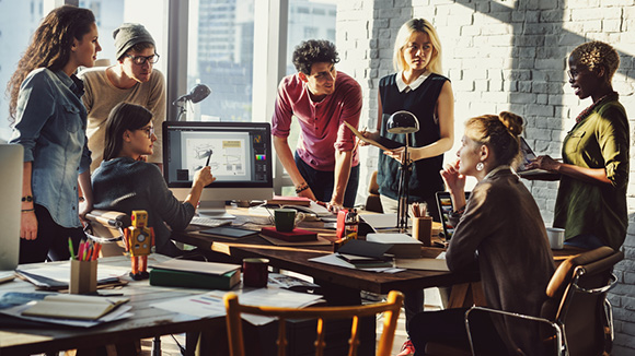 group of young people gathered around desk working and collaborating