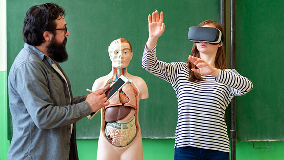 instructor with student wearing a VR headset with human anatomy mannequin in background