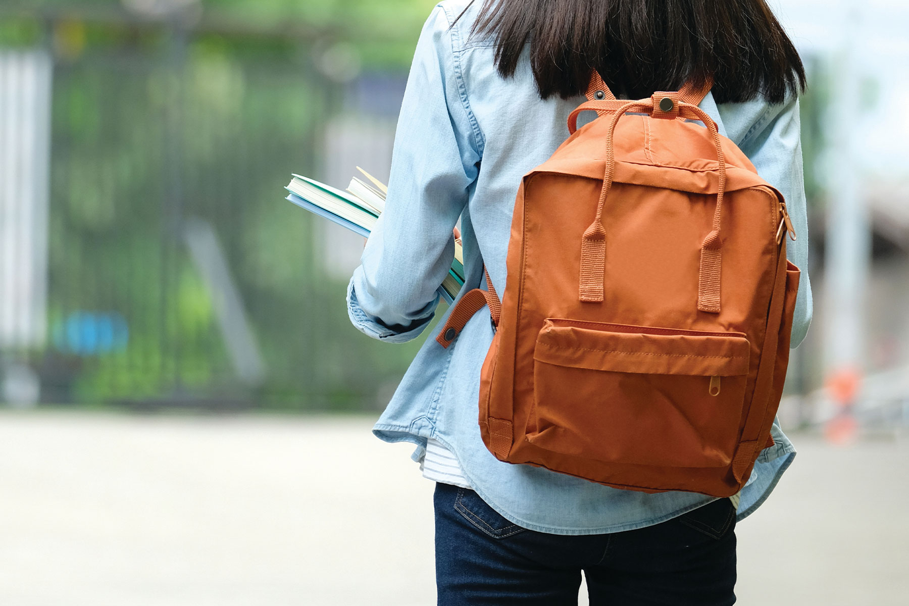 view of college student from behind, wearing backpack and holding books