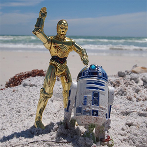action figures of C3P0 and R2D2 in the sand at the beach