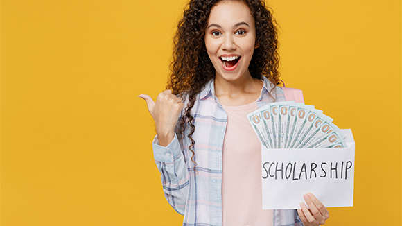 excited young female scholarship winner holds a fan of cash sticking out of an envelope that reads scholarship