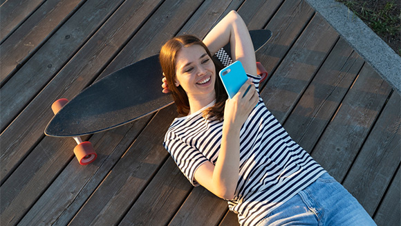 female college student laying down resting her head on a skateboard as she uses her phone