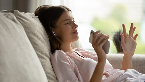 Content young woman leaning back on couch, stretching in relaxation with her phone in her hand and wearing headphones