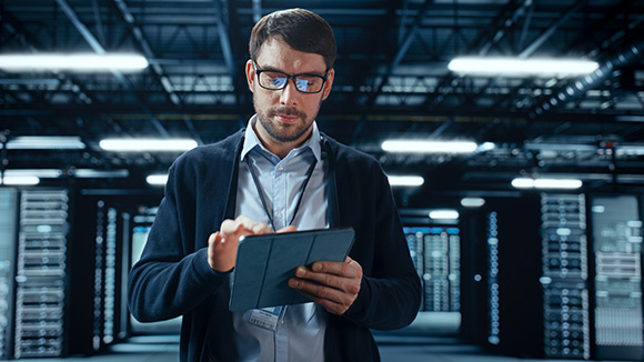 Male IT Specialist Walks Between Row of Operational Server Racks in Data Center