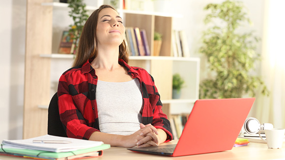 Relaxed student woman with red laptop breathing fresh air sitting at a desk at home