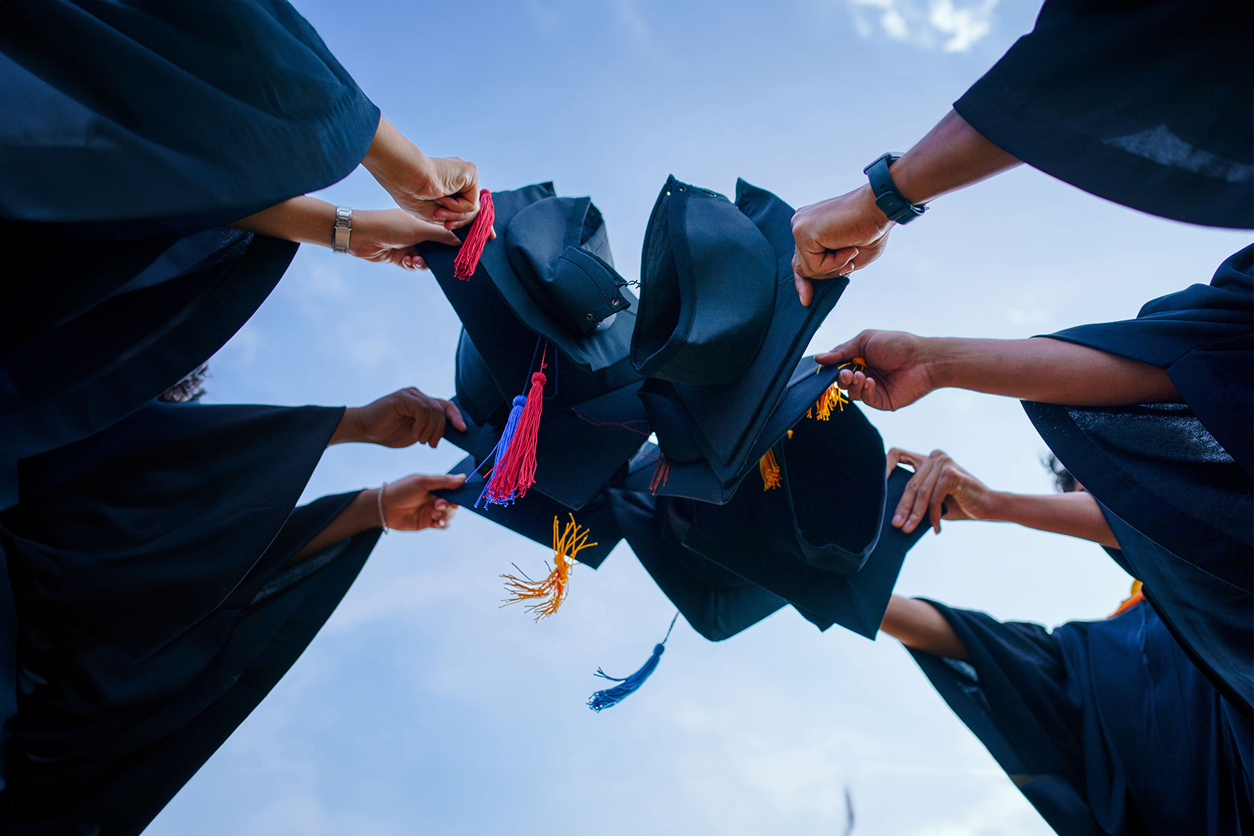 close up of group of graduates holding graduation hats together in a circle