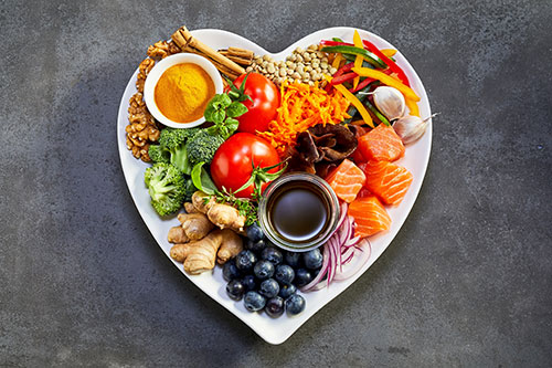 overhead view of a heart shaped plate full of healthy, nutritious fruits, vegetables, nuts, meats, and other options