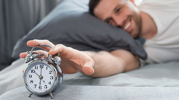 well rested man waking up and turning off his alarm clock