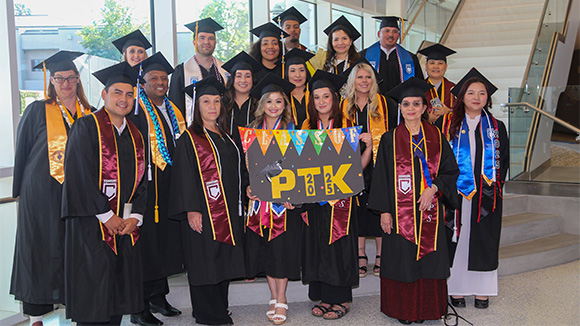 graduating phi theta kappa coastline students stand on the lobby steps of the student services center for a graduation photo